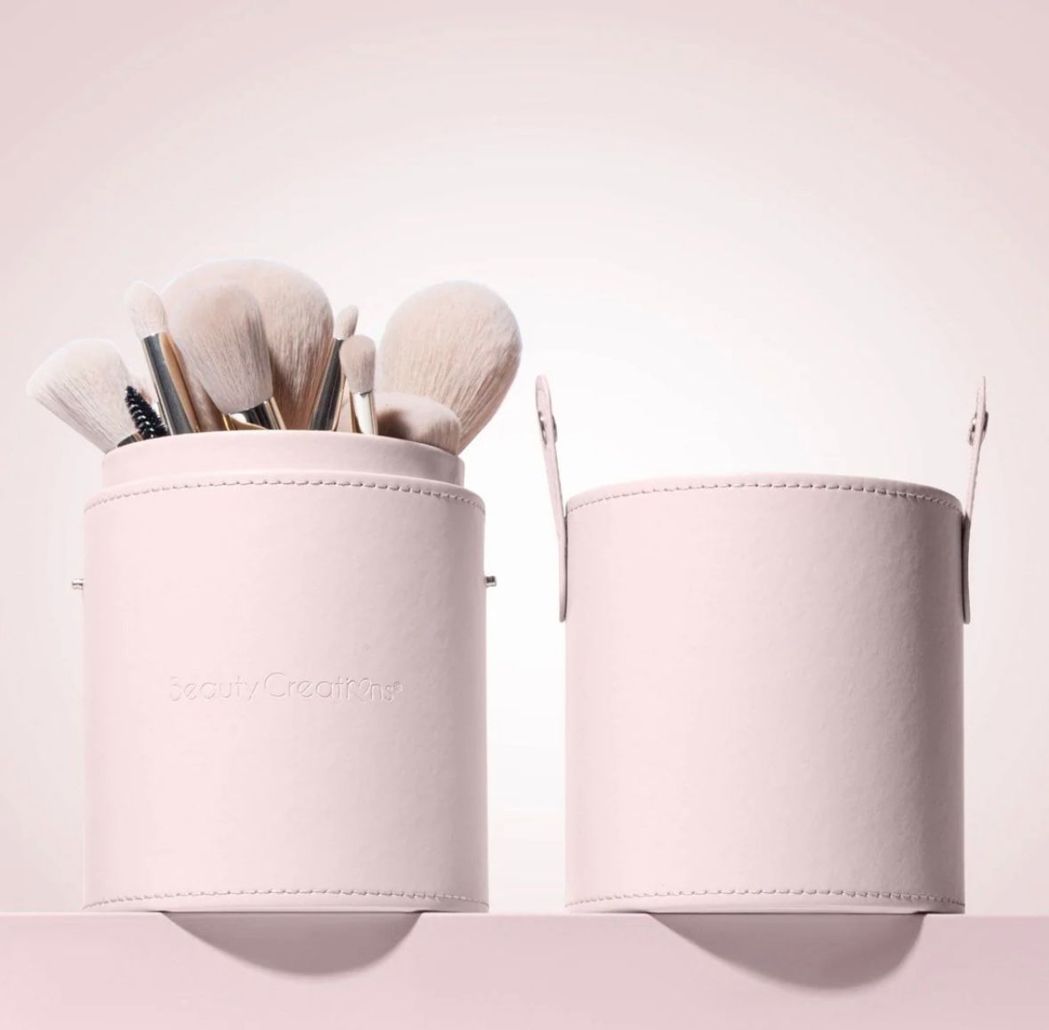 Two pink containers filled with makeup brushes on a shelf.