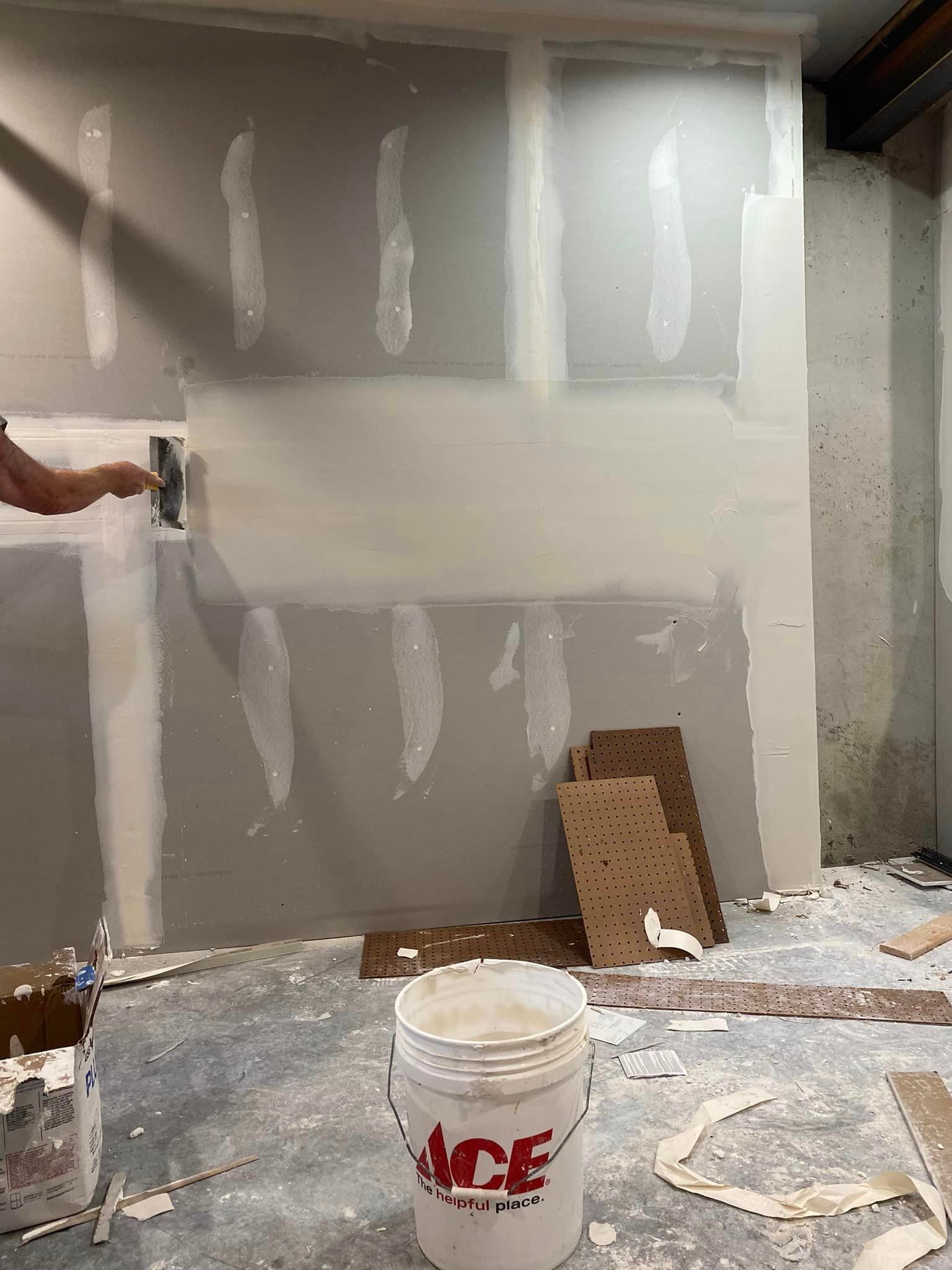 A person is painting a wall in a room with a bucket of ace paint.
