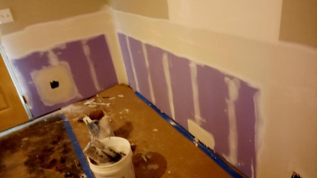 A bucket of paint is sitting on the floor next to a wall being painted.