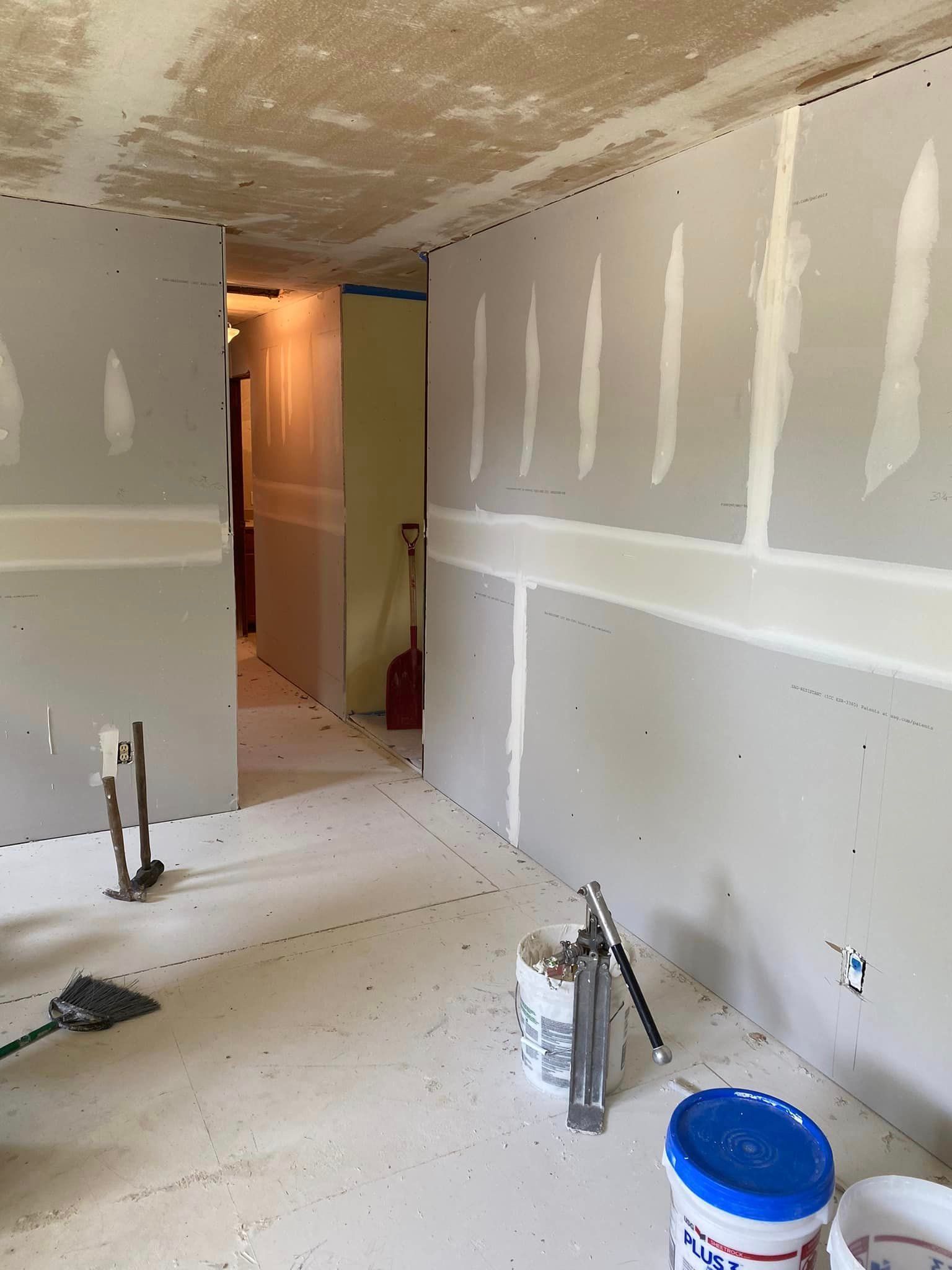 A room with drywall and a bucket of paint on the floor.