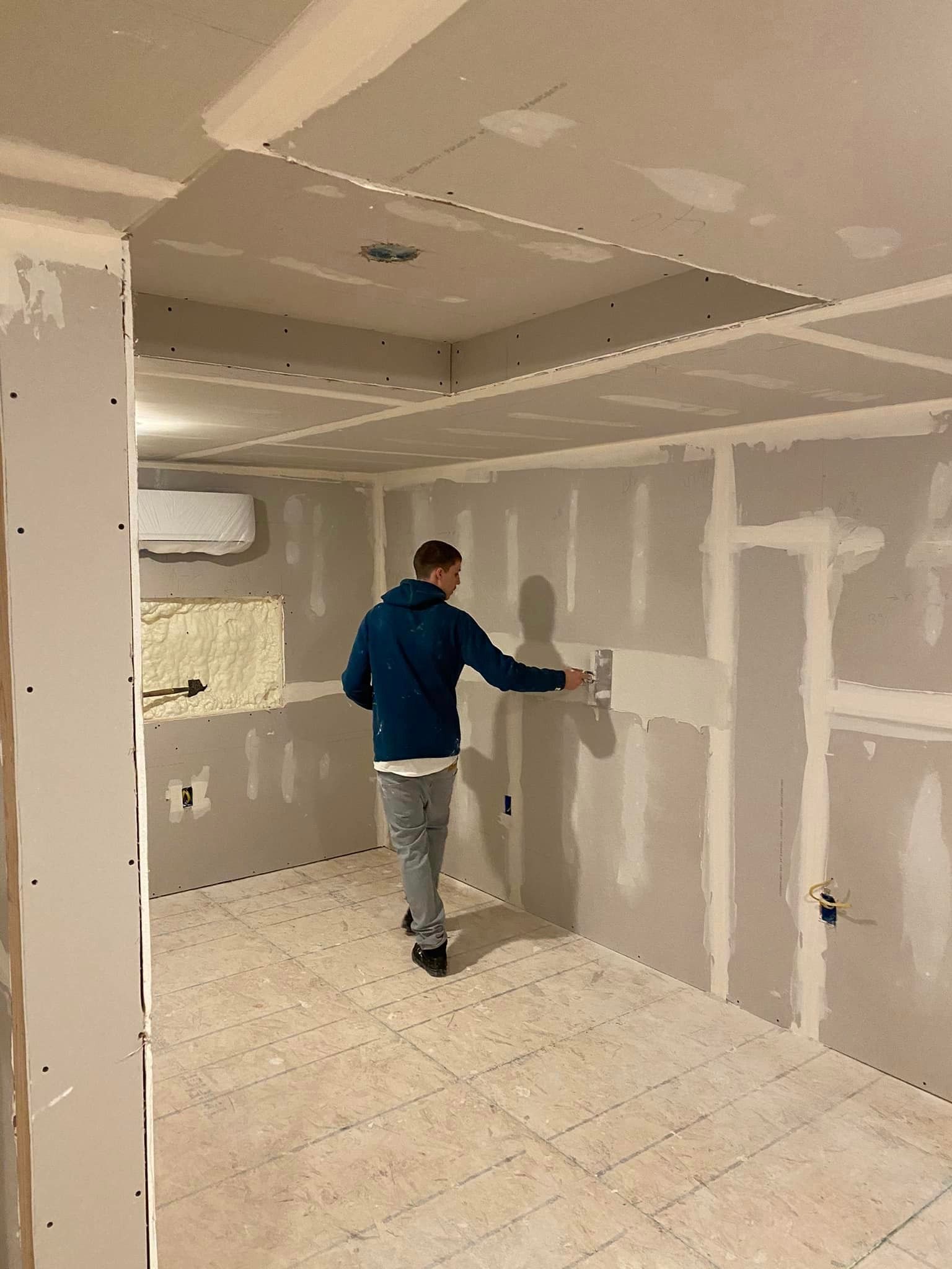 A man is plastering a wall in a room.