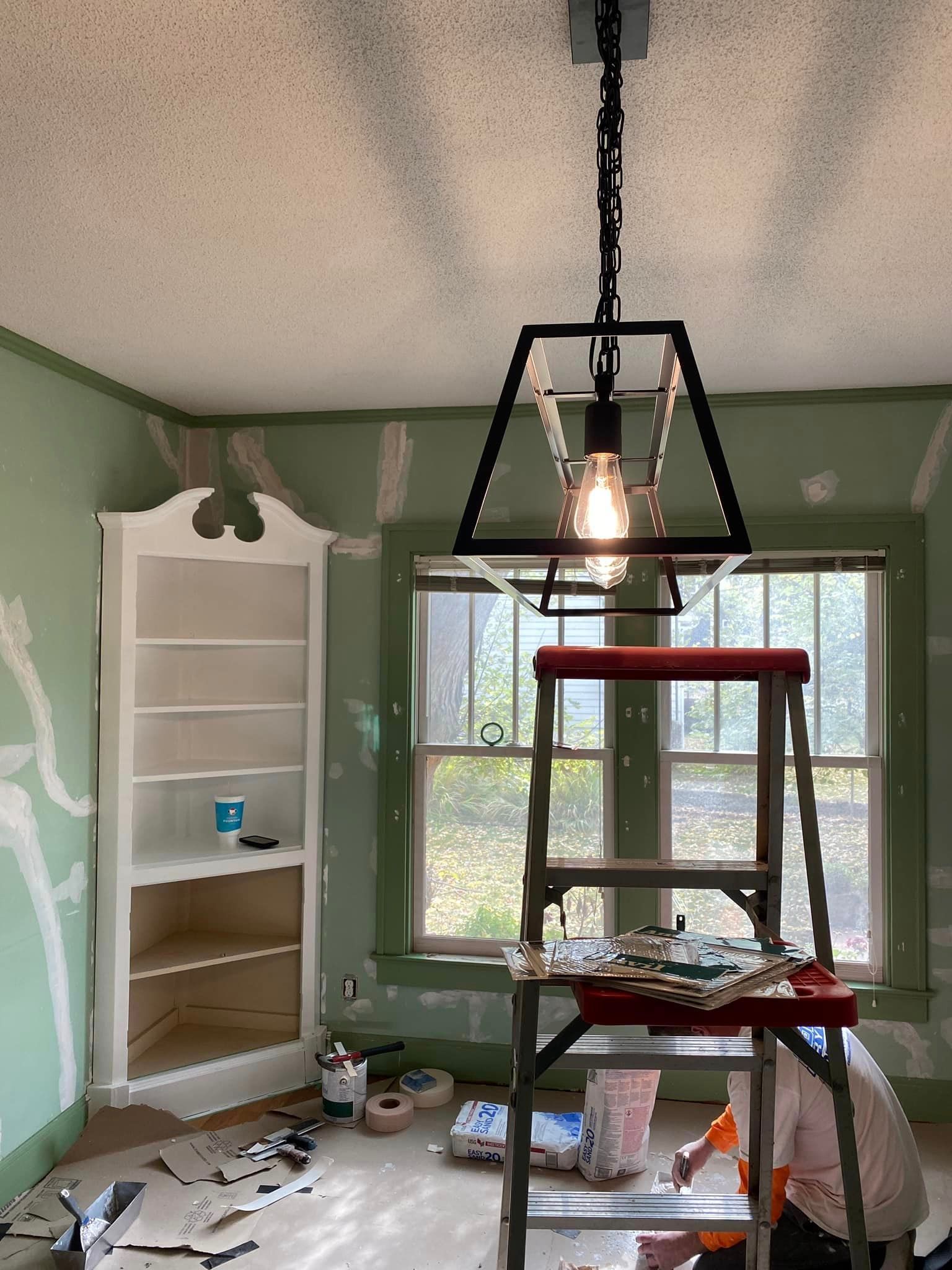 A man is sitting on a ladder in a room with a light hanging from the ceiling.