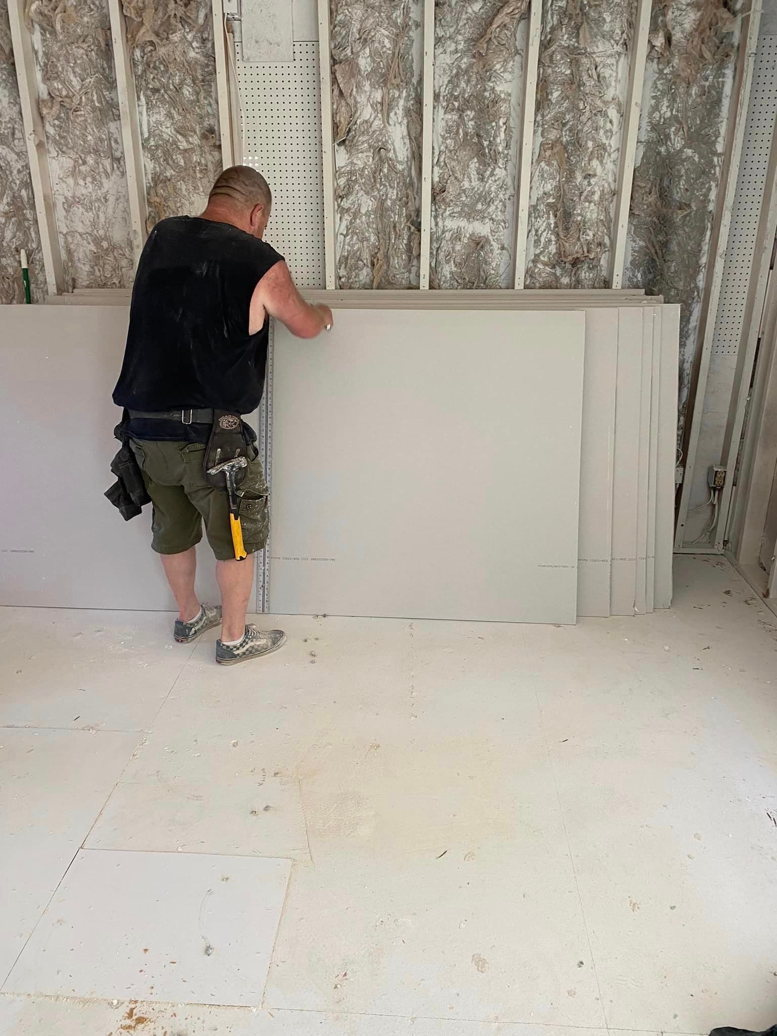 A man is standing next to a large piece of drywall in a room.