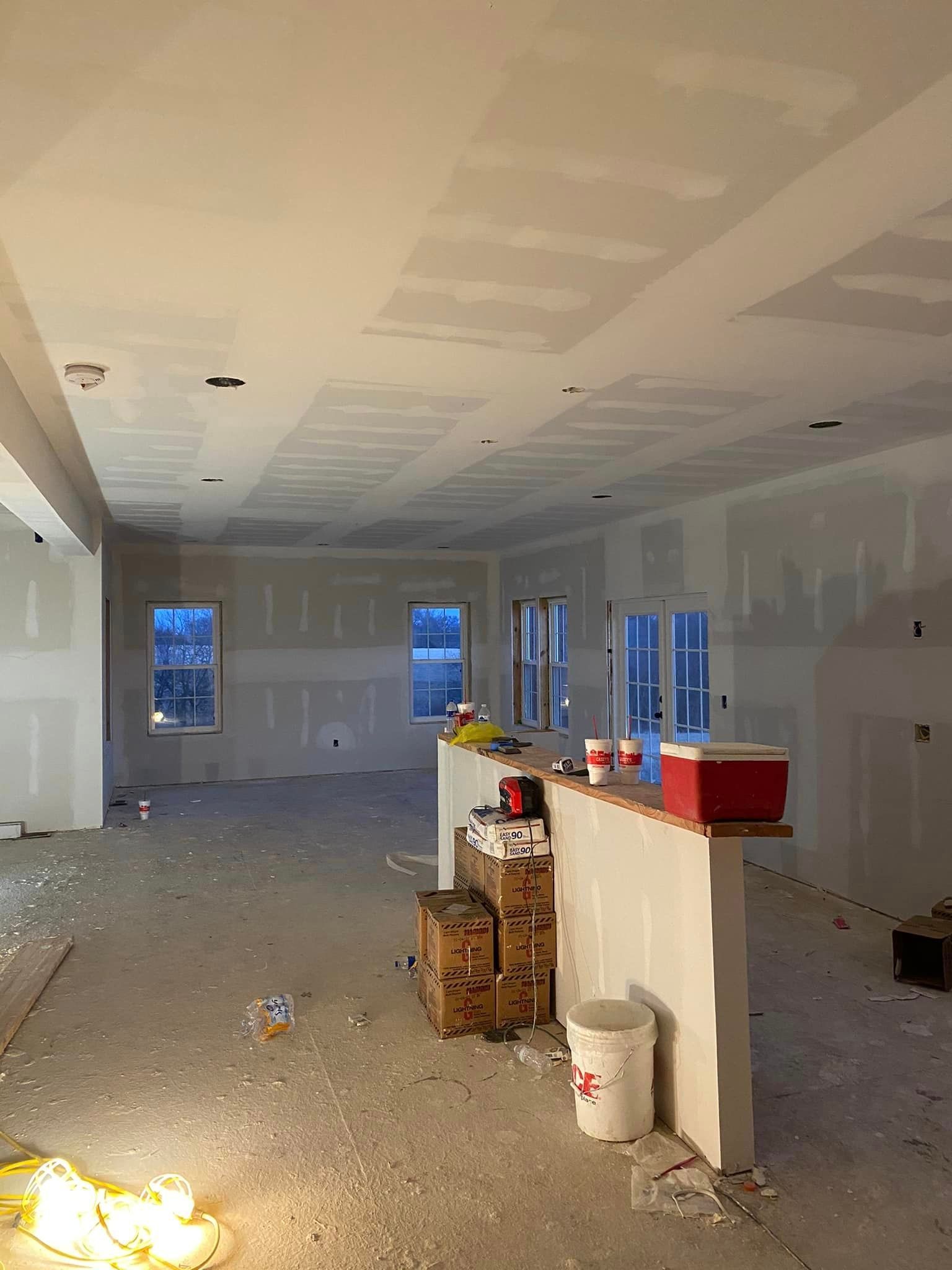 A large empty room with drywall on the walls and a bucket on the floor.