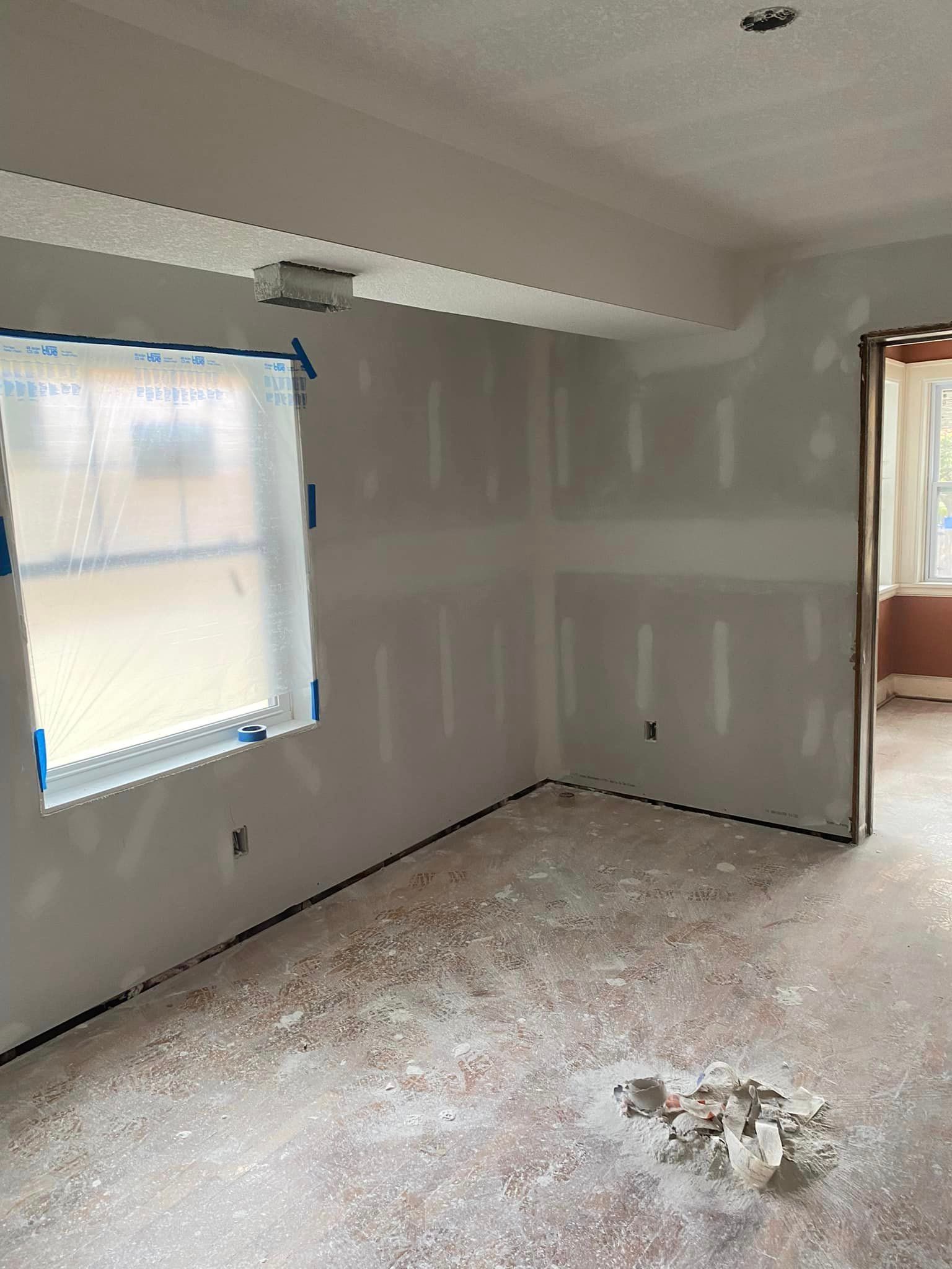 An empty room with a window and drywall on the walls.