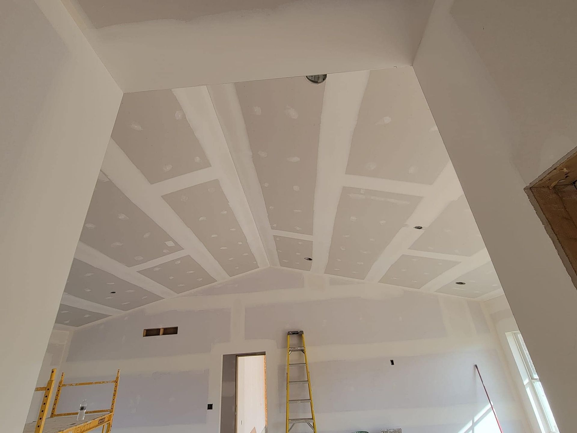 A room with a vaulted ceiling and a ladder in it.