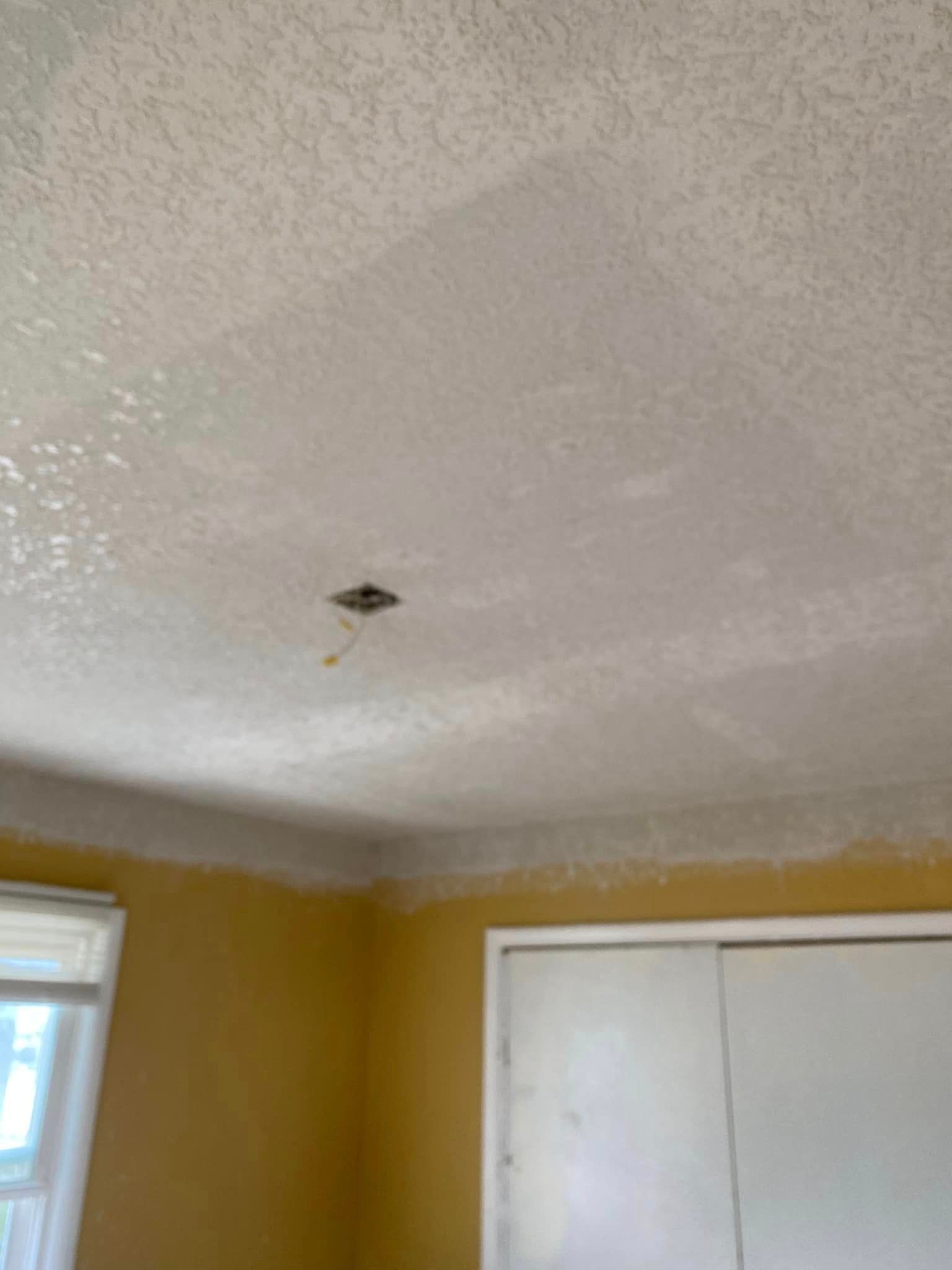 A room with yellow walls and a white ceiling with a hole in it.