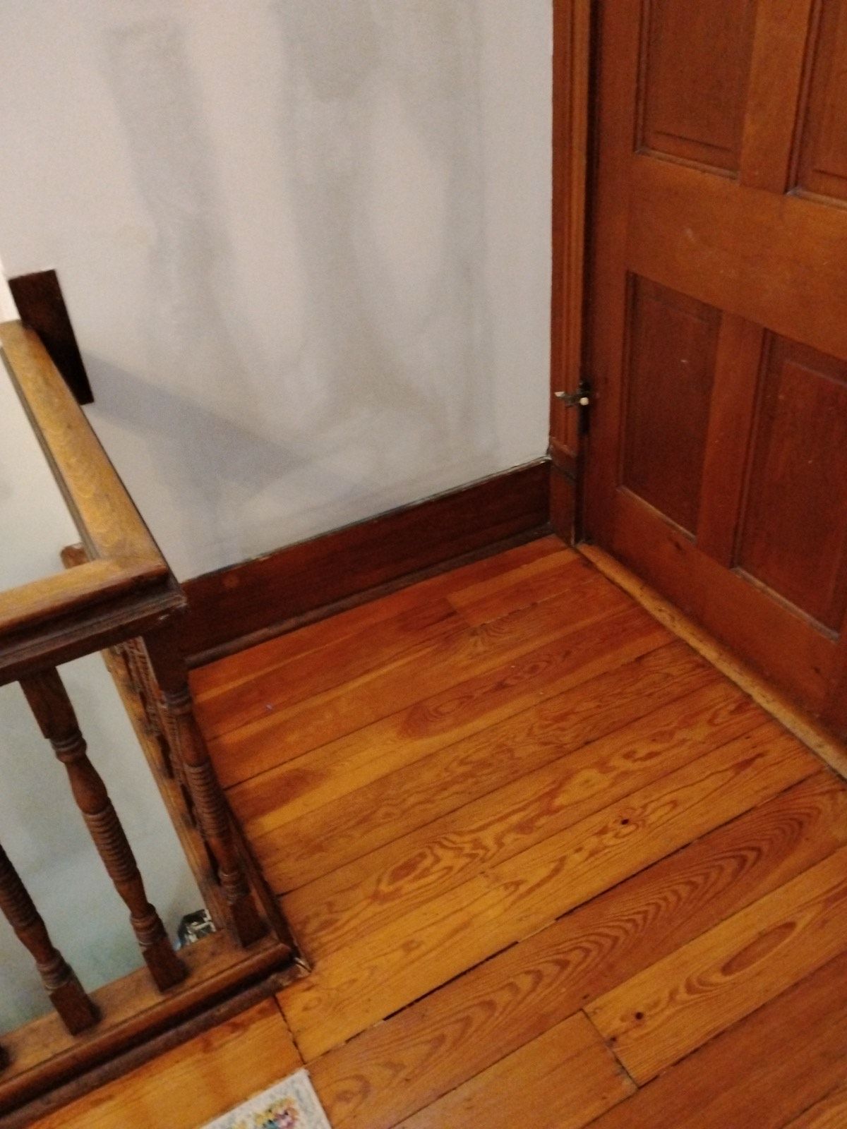 A wooden floor in a room next to a door and stairs.