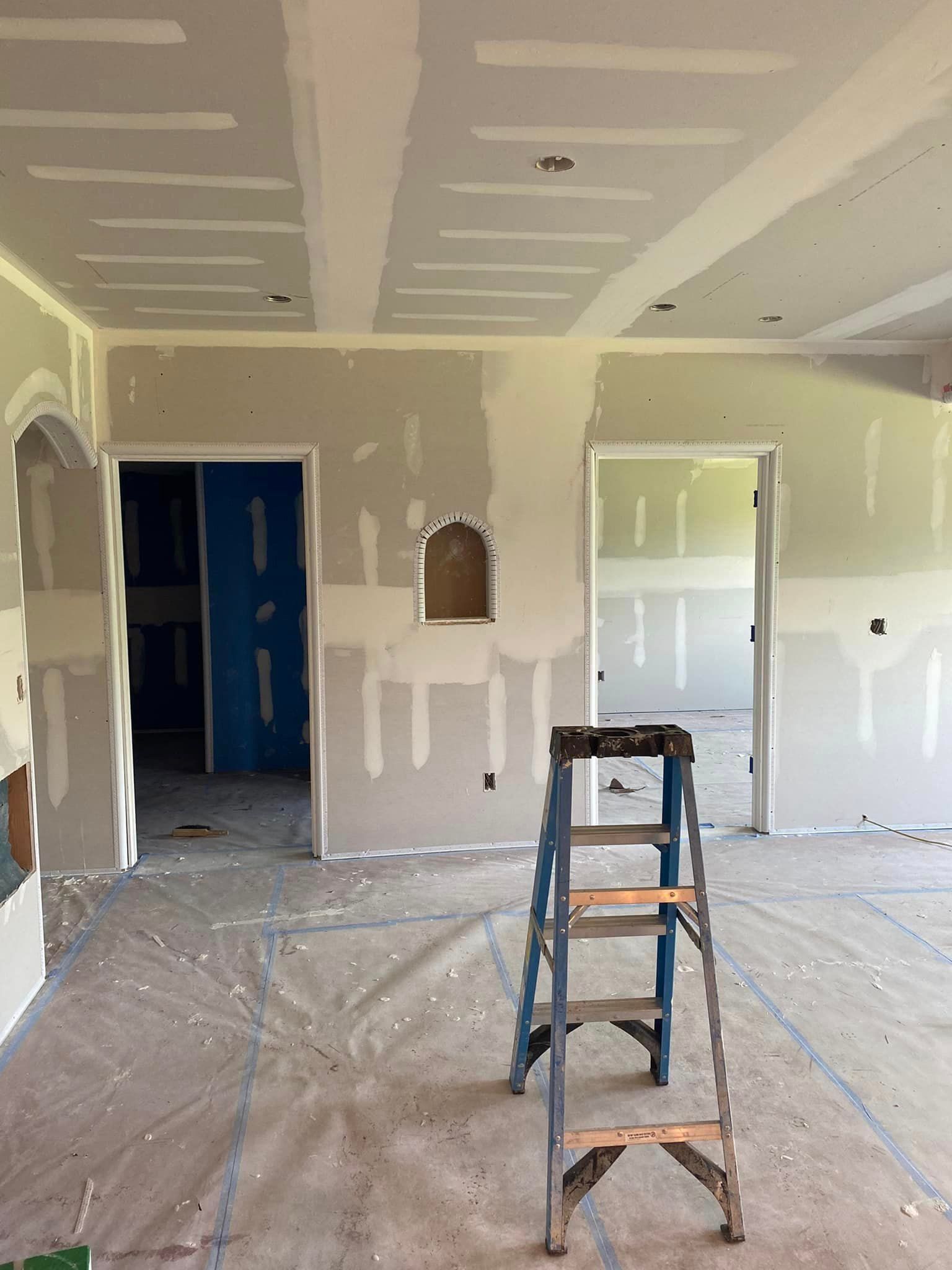 A ladder is sitting in the middle of a room that is being painted.
