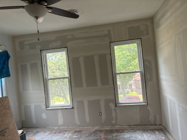 A room with a ceiling fan and three windows.
