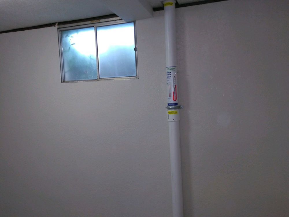 A room with a window and a white pipe on the wall.