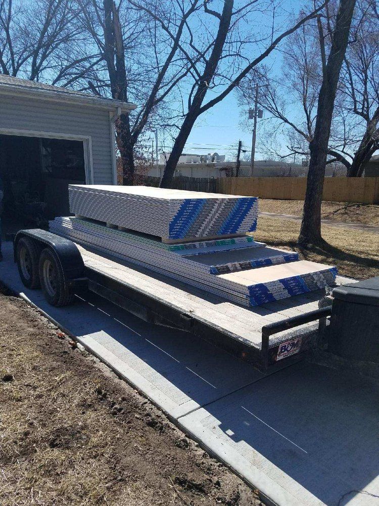 A trailer filled with a bunch of boxes is parked in front of a garage.