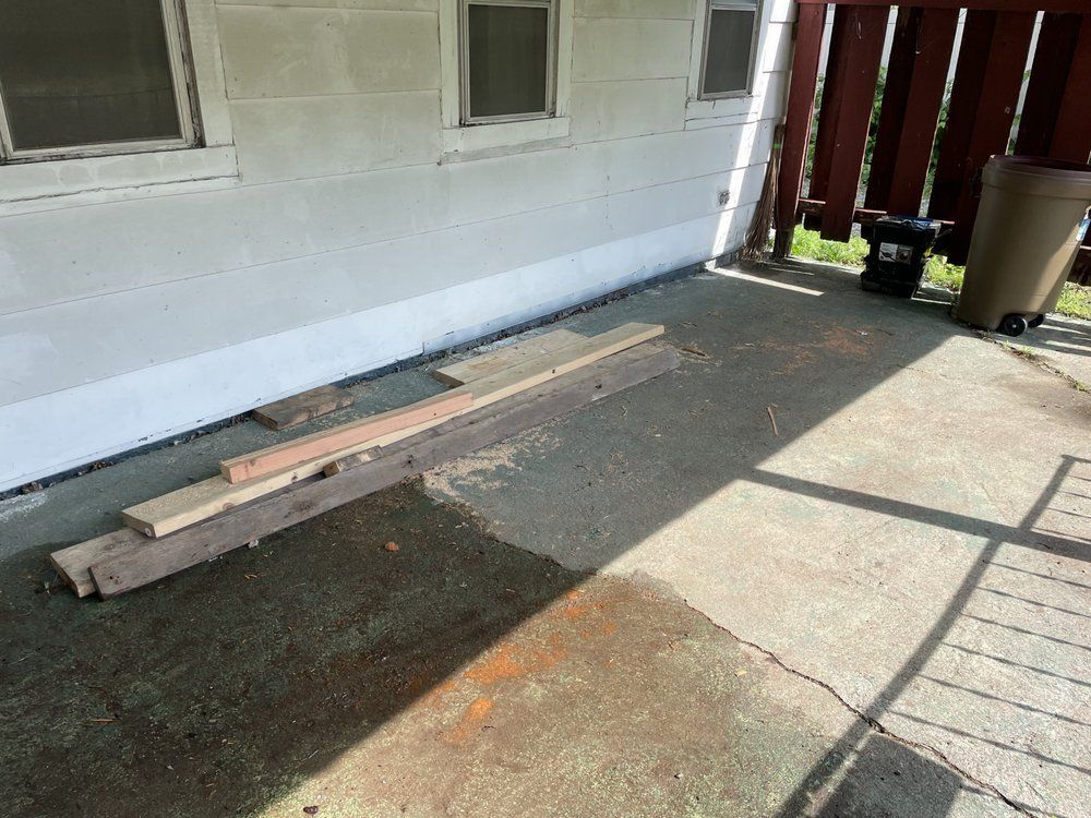 A pile of wood is sitting on the ground in front of a house.