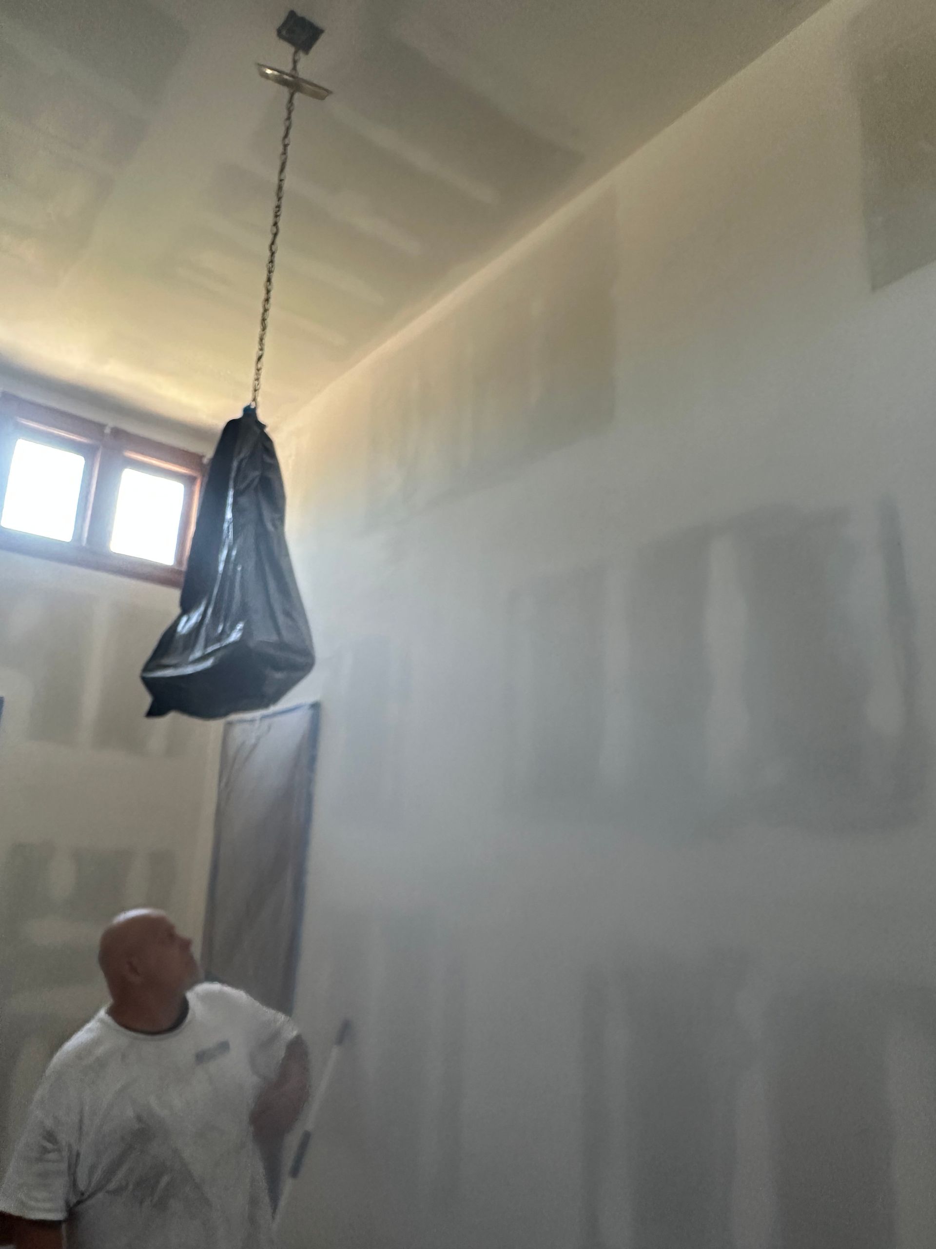 A man is standing in a room with a bag hanging from the ceiling.