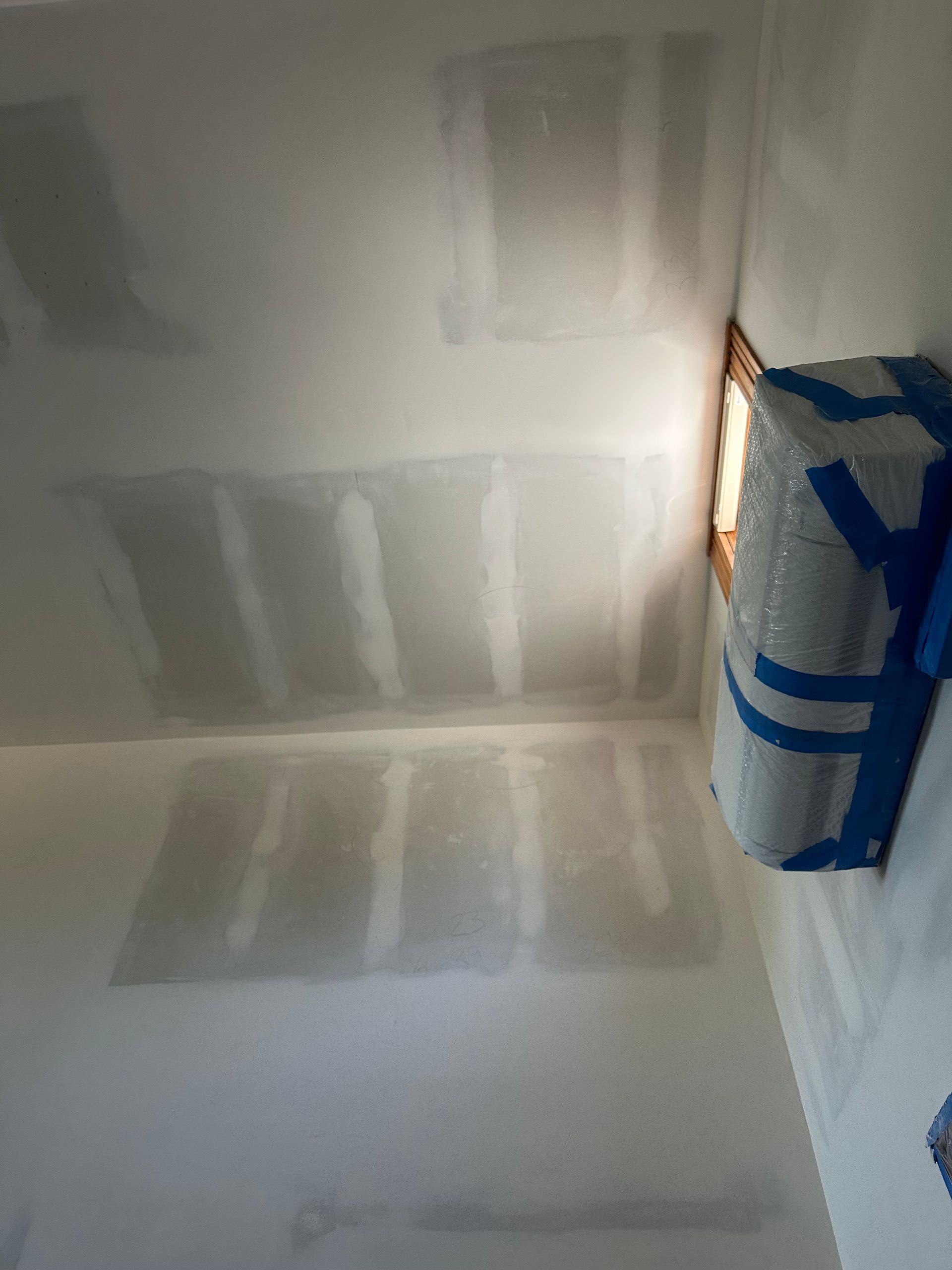 A room with a ceiling that is being painted and a bag of packing tape on the wall.