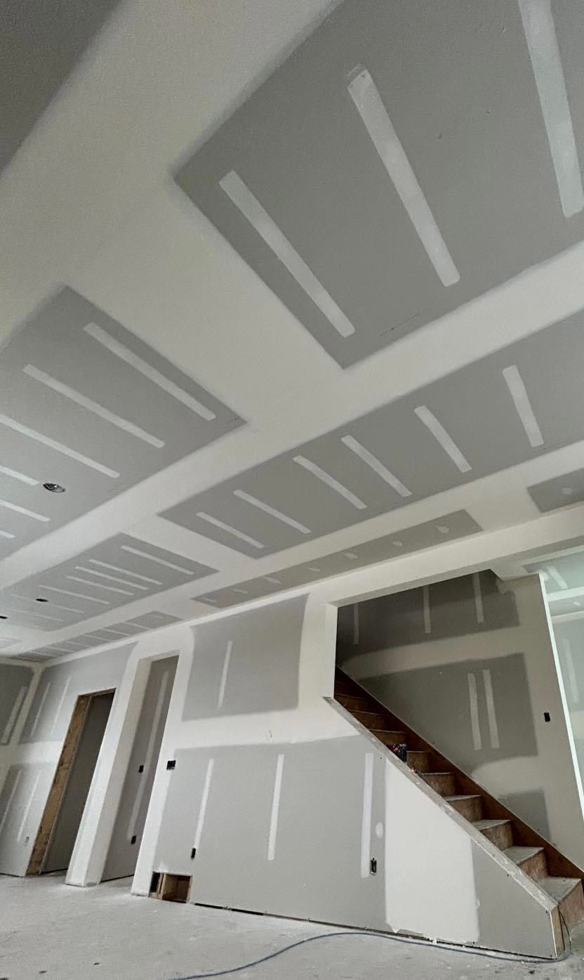 A room with a staircase and drywall on the ceiling.