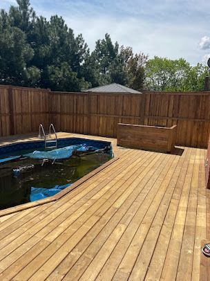 A wooden deck next to a swimming pool surrounded by a wooden fence.