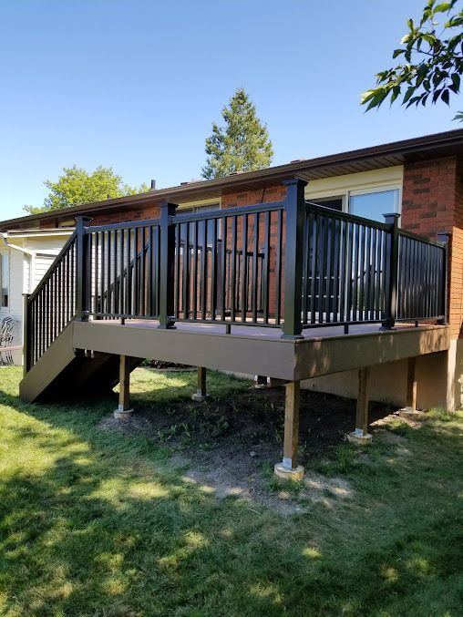 A large deck with stairs leading up to it is in front of a brick house.