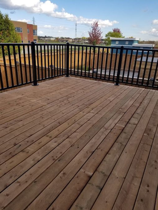 A wooden deck with a black railing and a view of a city.