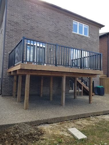 A large wooden deck with stairs is in the backyard of a brick house.