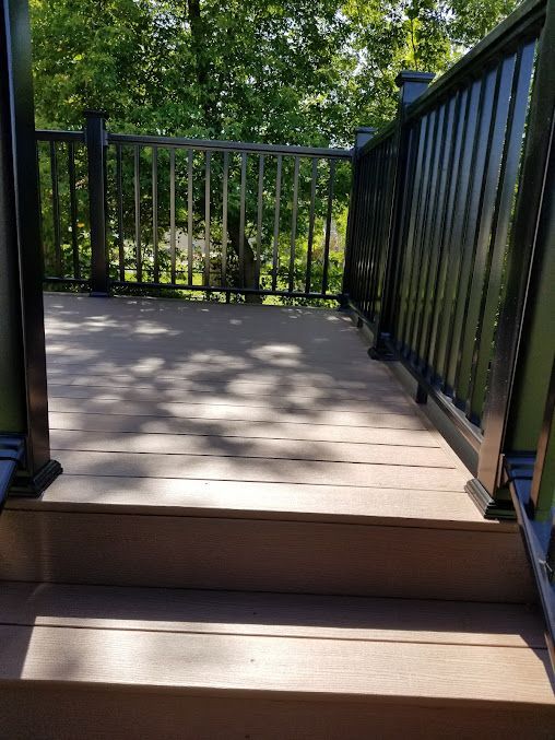 A wooden deck with stairs leading up to it and a black railing.