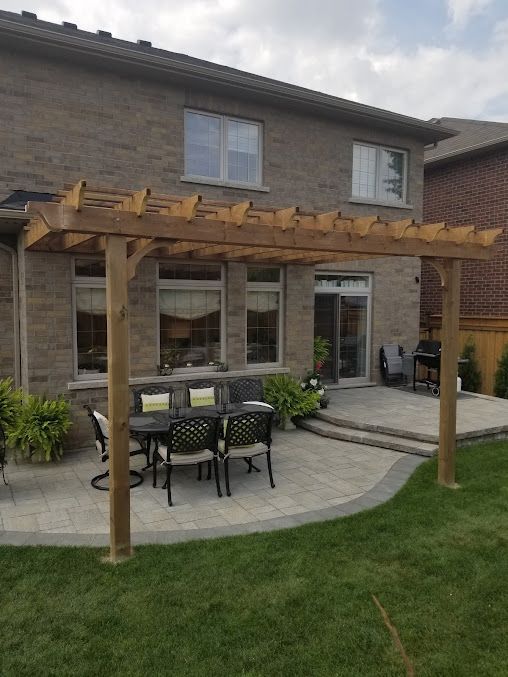 A patio with a pergola and a table and chairs in front of a brick house
