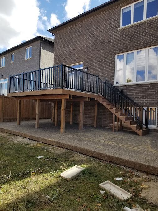 A wooden deck with stairs leading up to it is in front of a brick house.