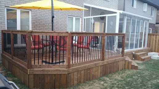 A wooden deck with a yellow umbrella and chairs in front of a house.