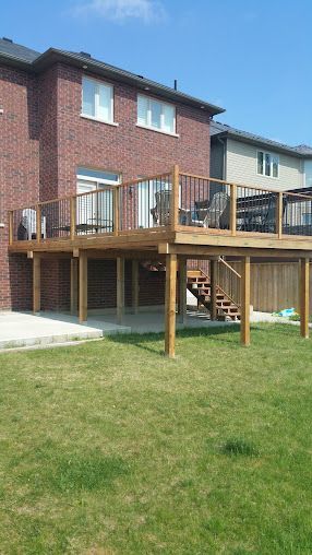 A wooden deck with stairs is in the backyard of a brick house.