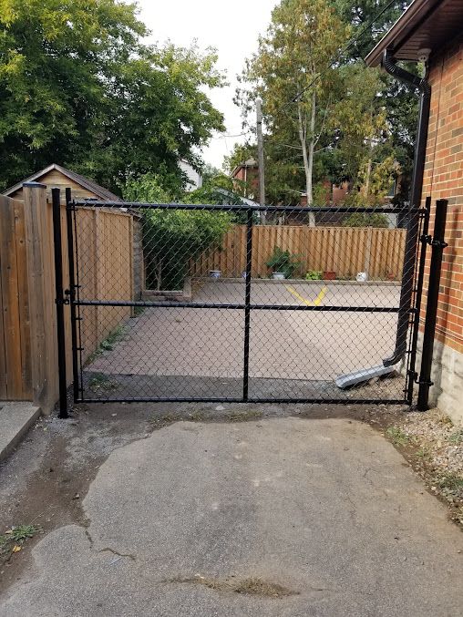 A chain link fence is surrounding a driveway in front of a brick house.