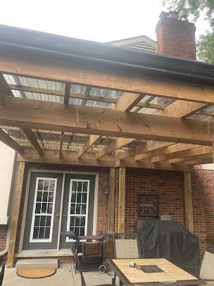 A wooden pergola is sitting on top of a patio next to a brick house.
