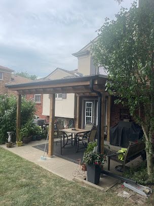 A patio with a table and chairs under a pergola in the backyard of a house.