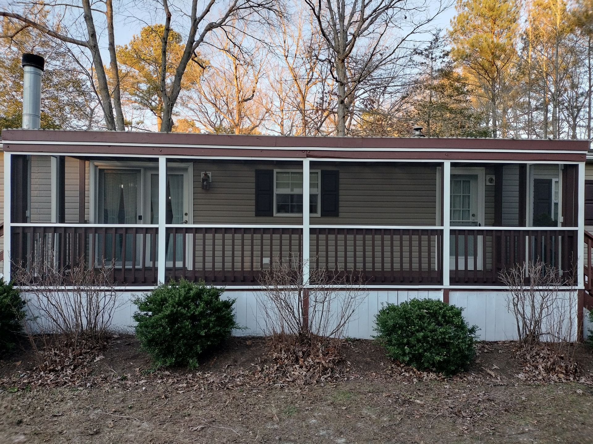 A mobile home with a screened in porch and trees in the background.