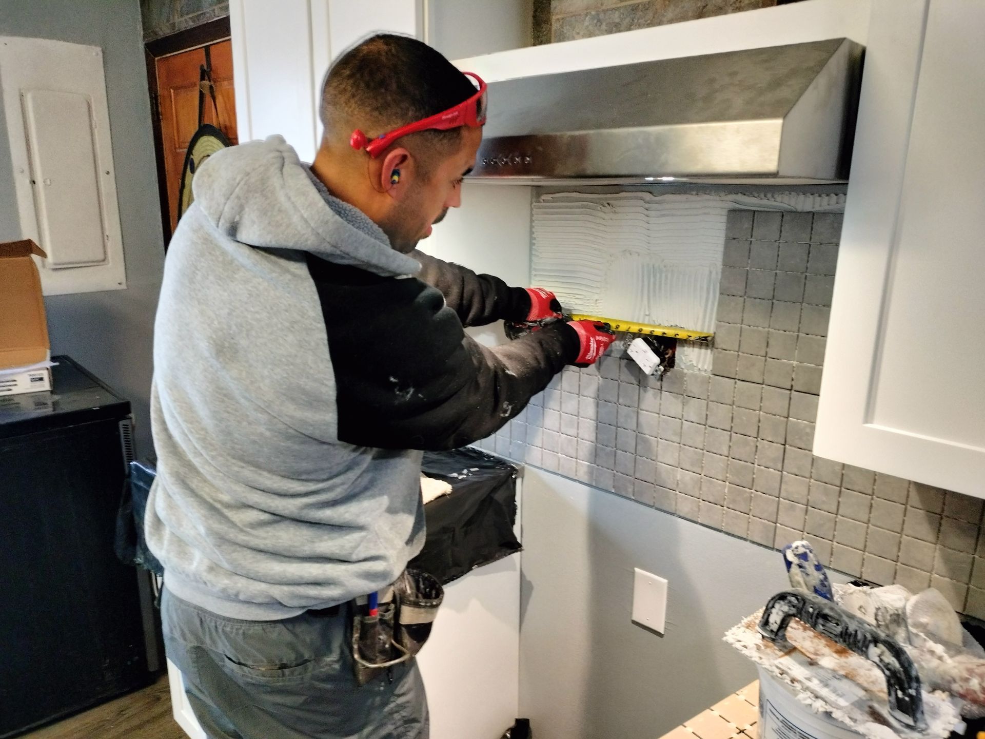 A man is measuring a wall in a kitchen with a tape measure.