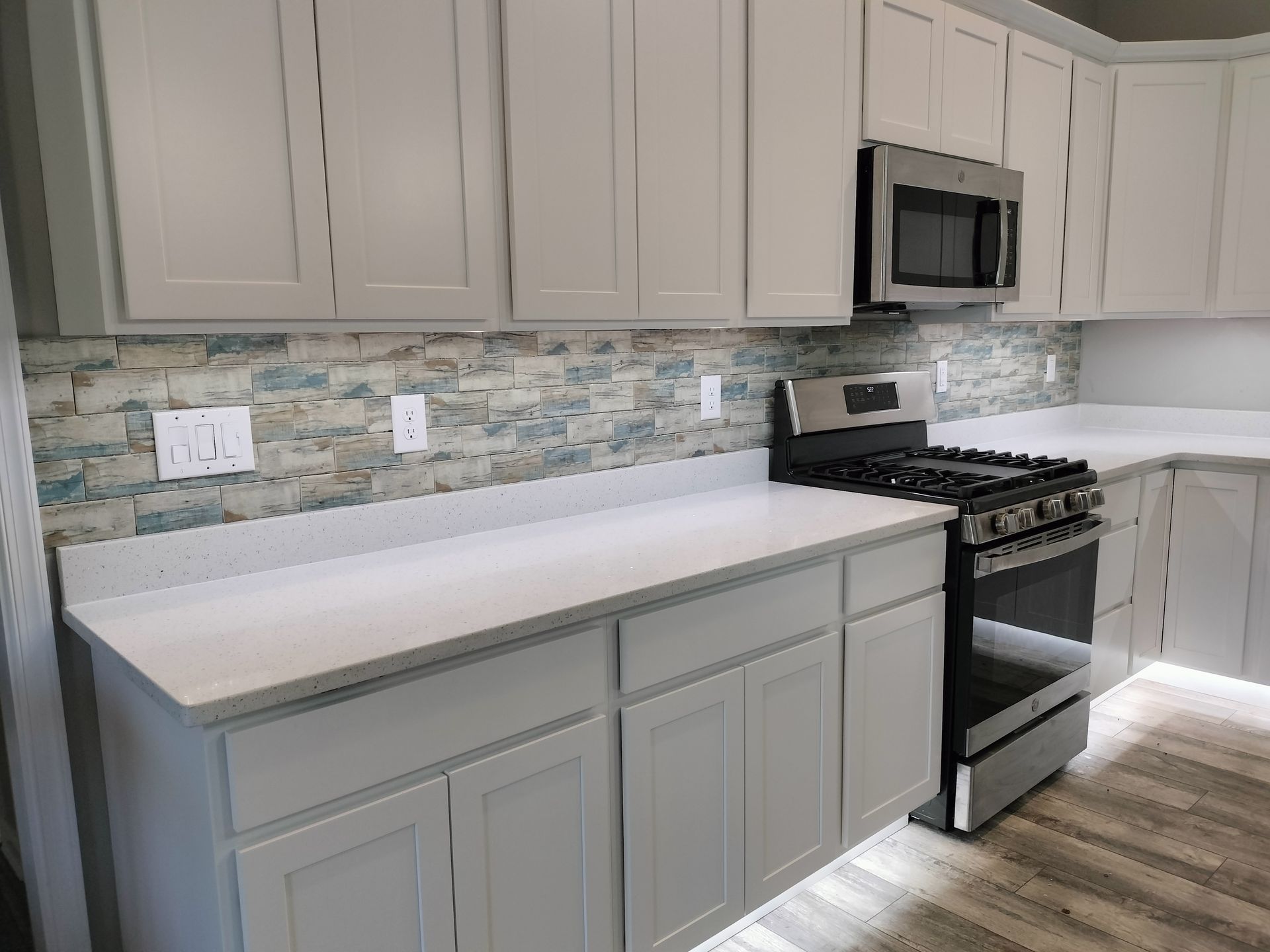 A kitchen with white cabinets , a stove , and a microwave.