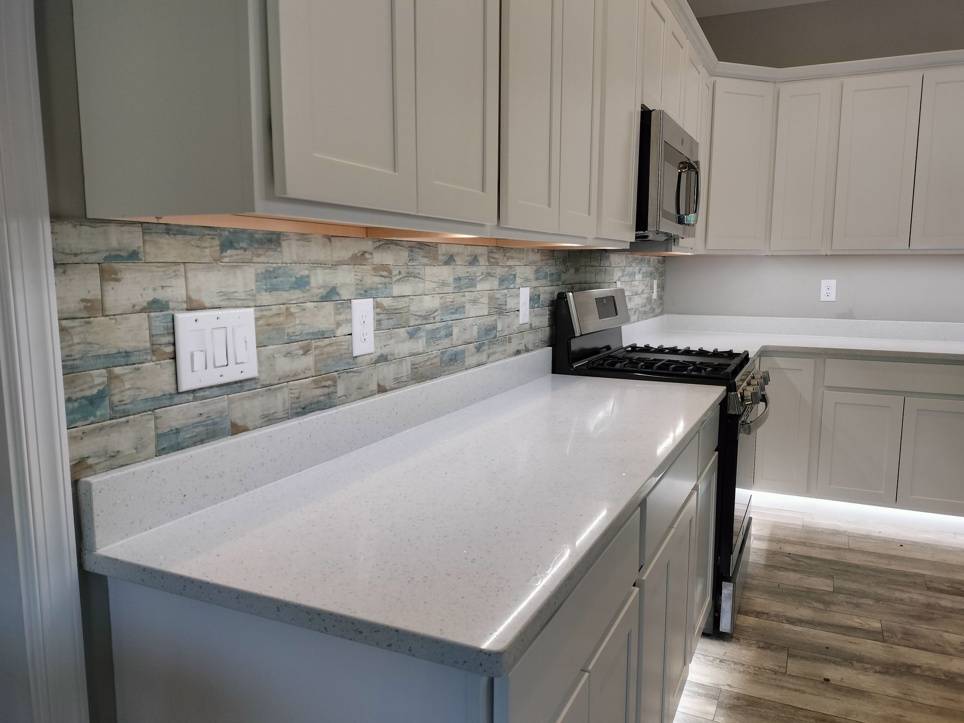 A kitchen with white cabinets , white counter tops , a stove and a microwave.