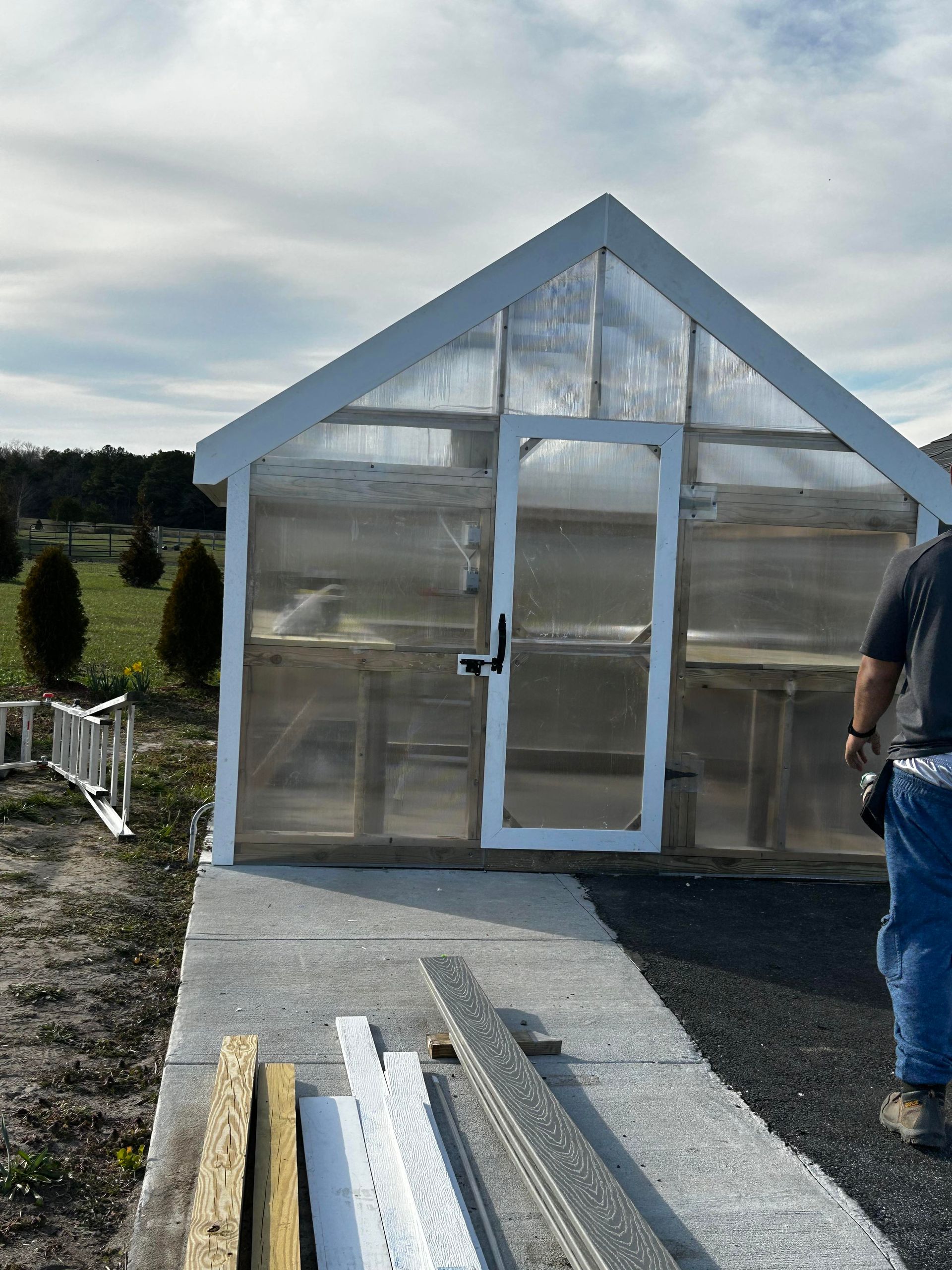 A man is standing in front of a greenhouse that is being built