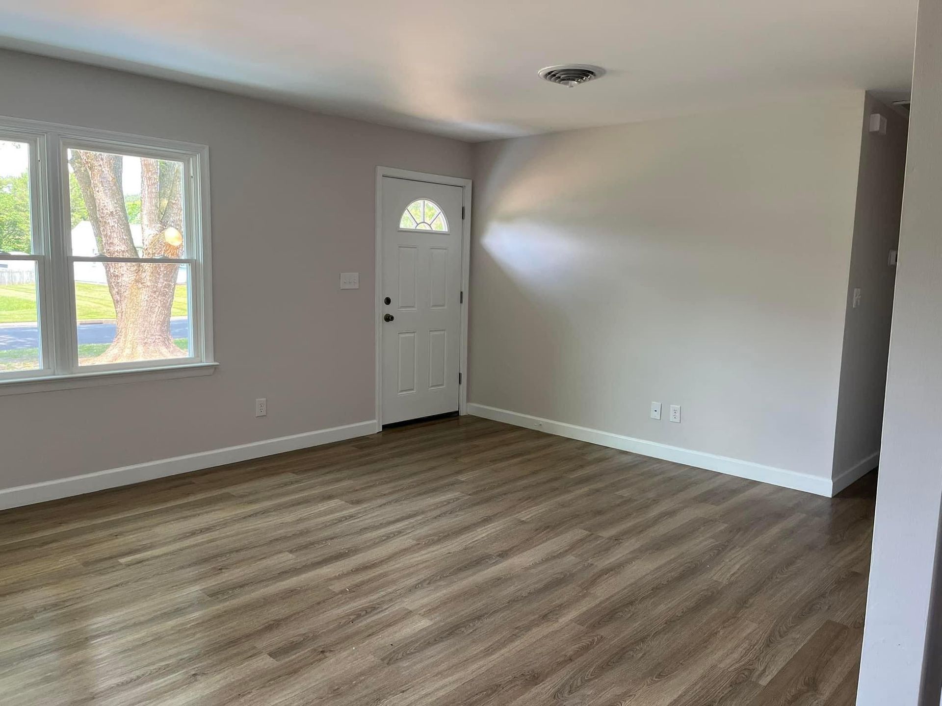 An empty living room with hardwood floors and a white door.