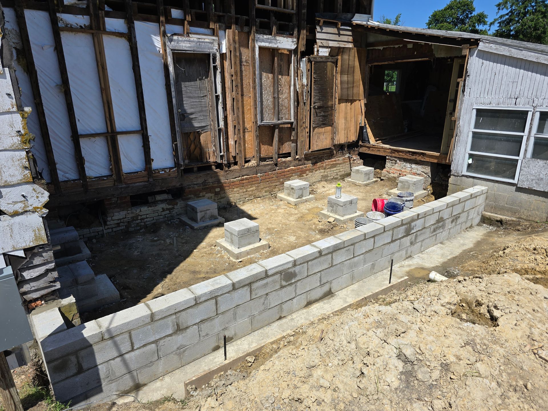 A brick wall is being built in front of a house that is being demolished.