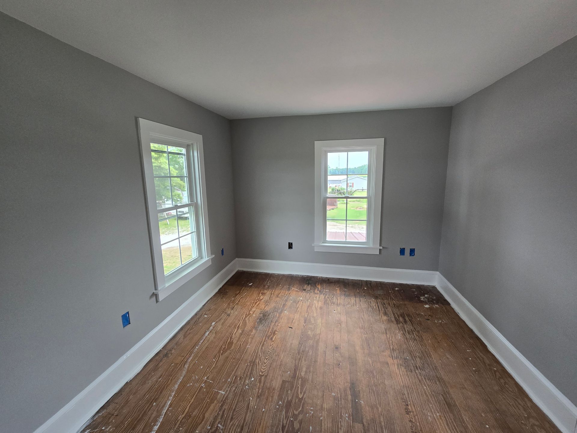 An empty room with a wooden floor and two windows.