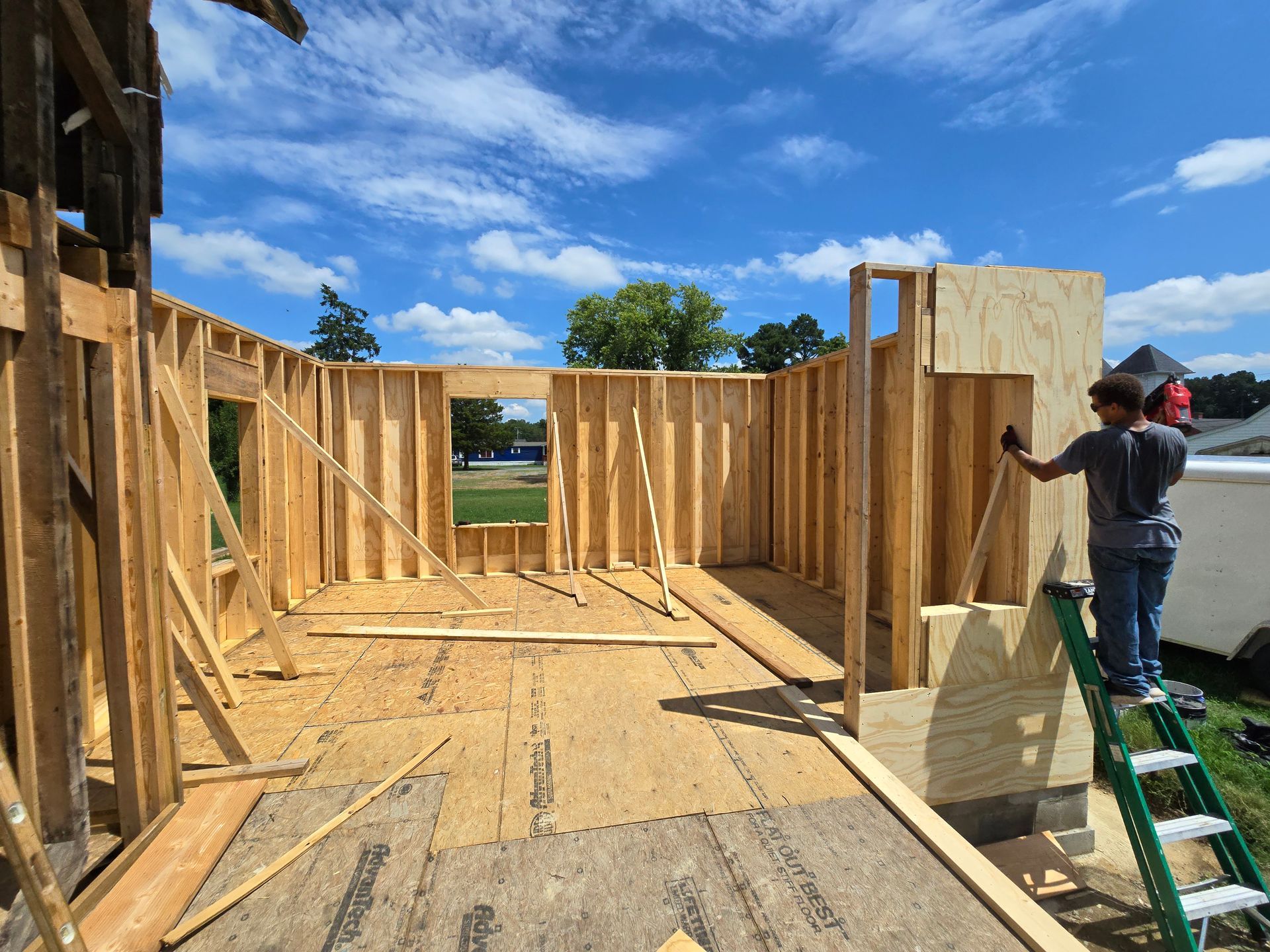 A man is standing on a ladder in front of a building under construction.