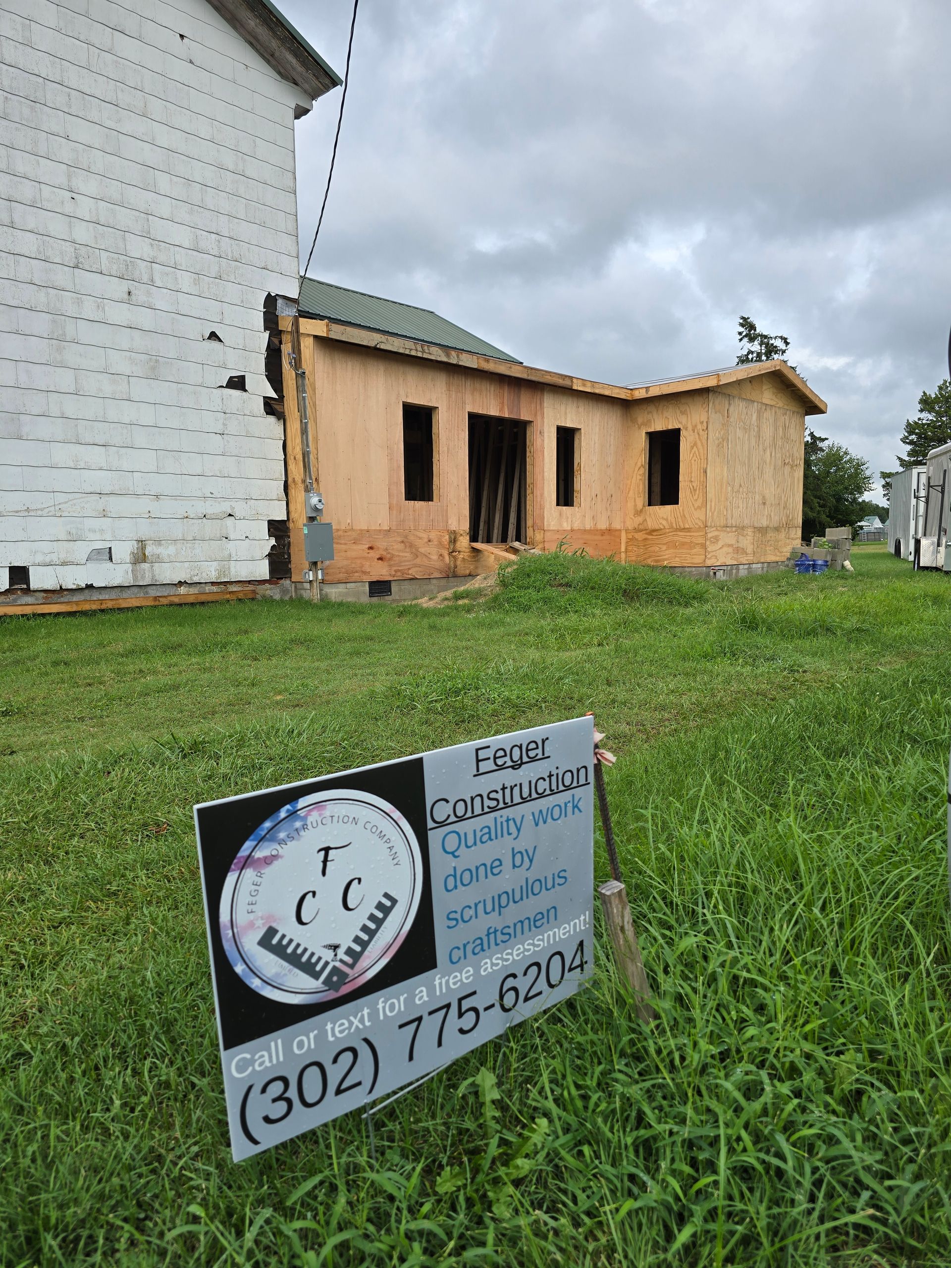 A sign is sitting in the grass in front of a house under construction.