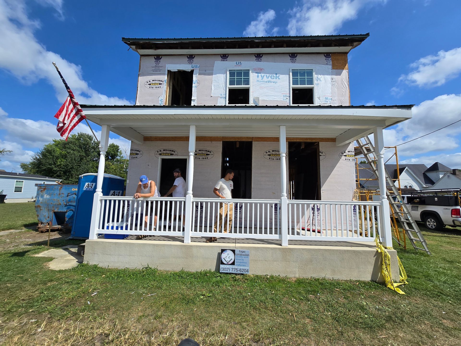 A group of people are standing on a porch of a house under construction.