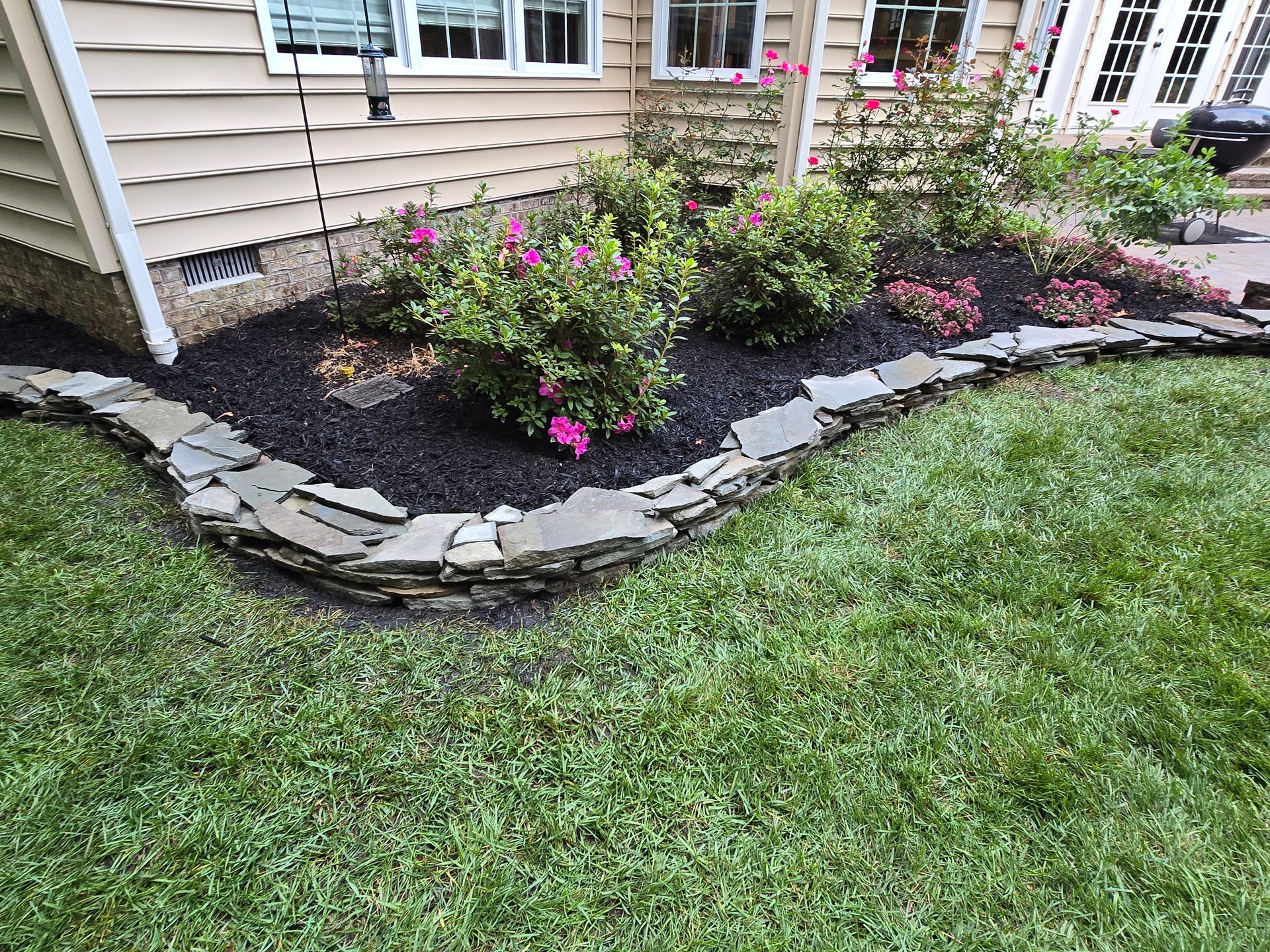 A lawn with flowers and rocks in front of a house.