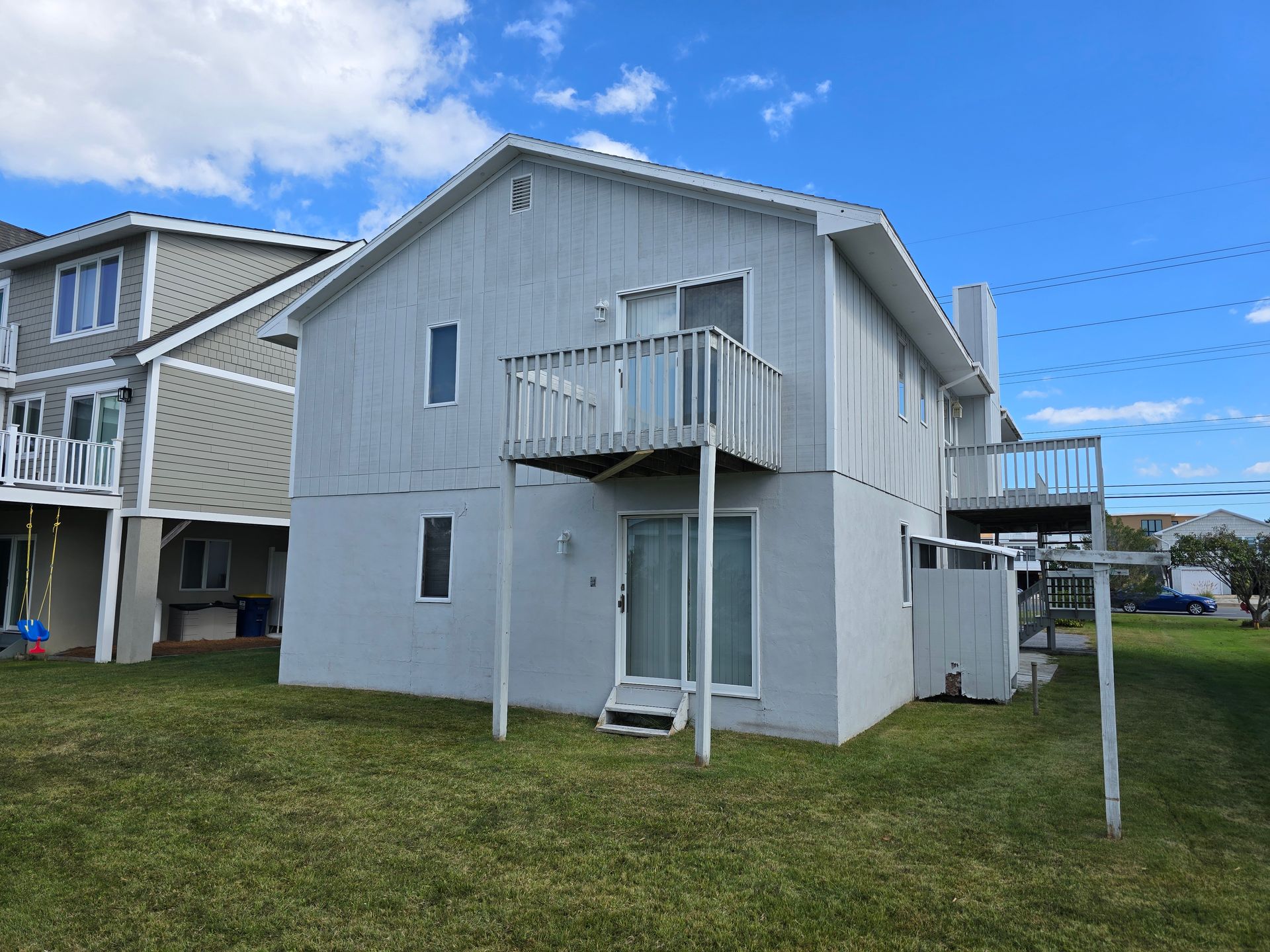 A white house with a balcony is sitting on top of a lush green field.