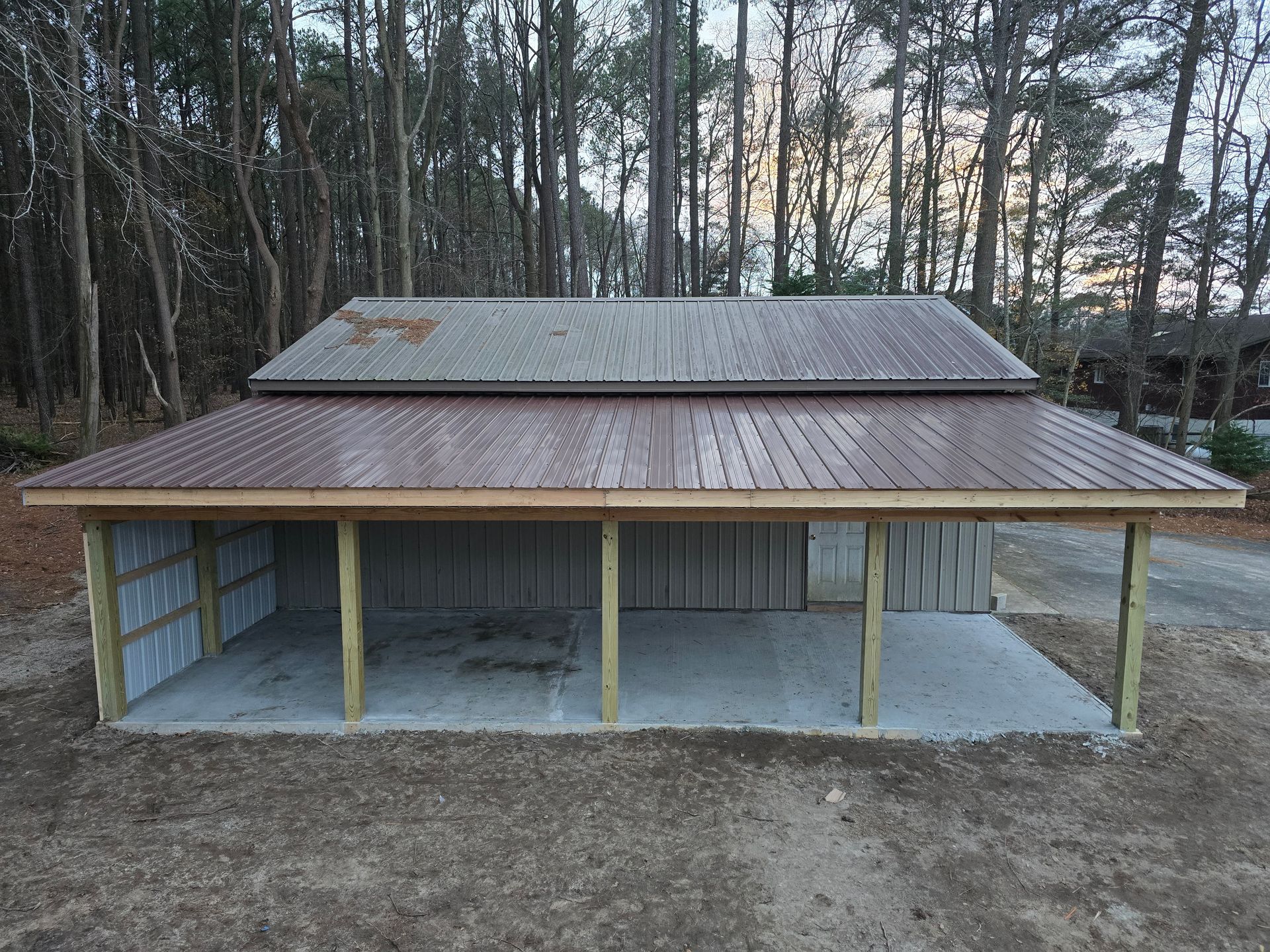 A garage with a metal roof and wooden posts in the middle of a forest.