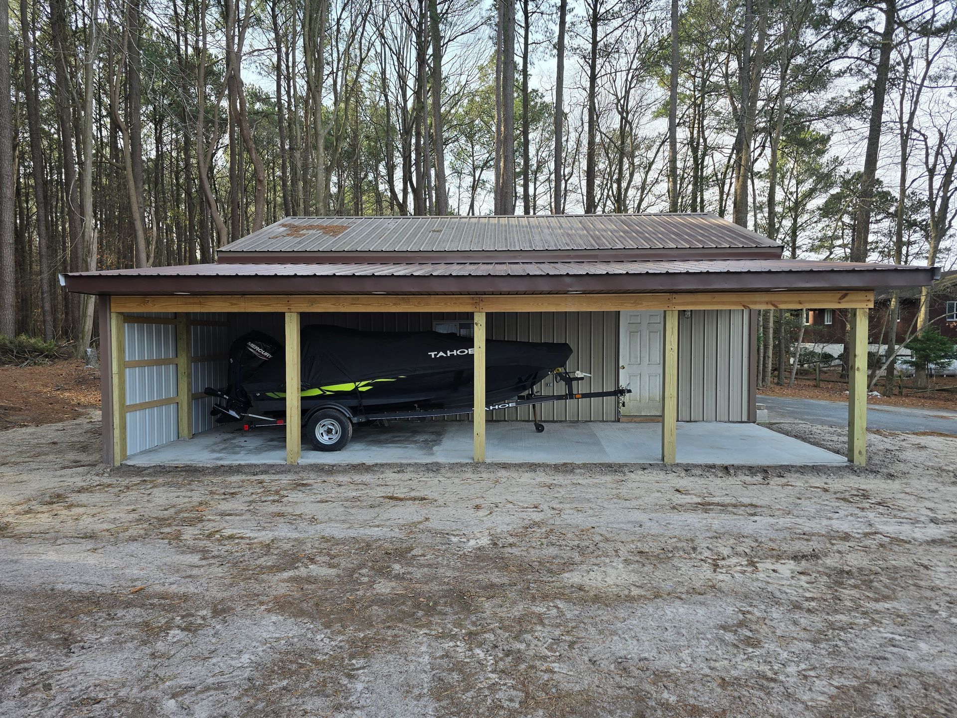 A boat is parked under a shed in the woods.