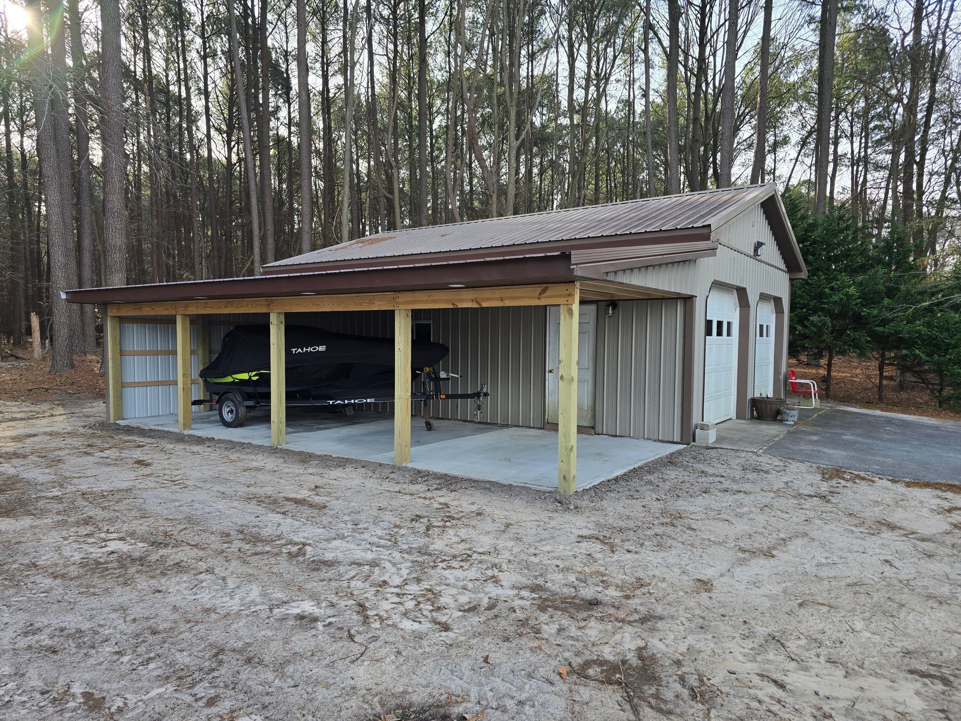 A boat is parked under a covered garage in the woods.