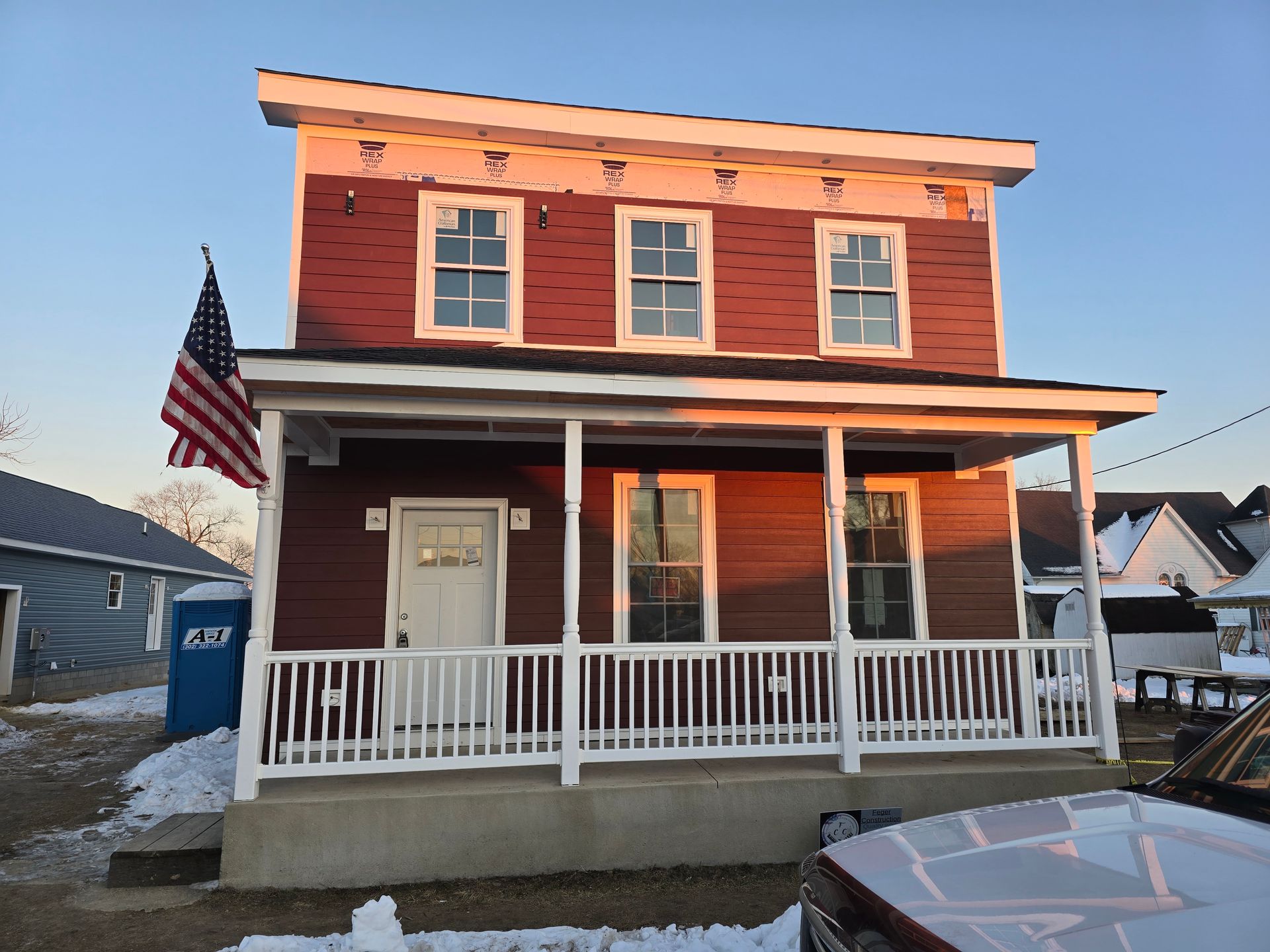 A red house with a white porch and an american flag