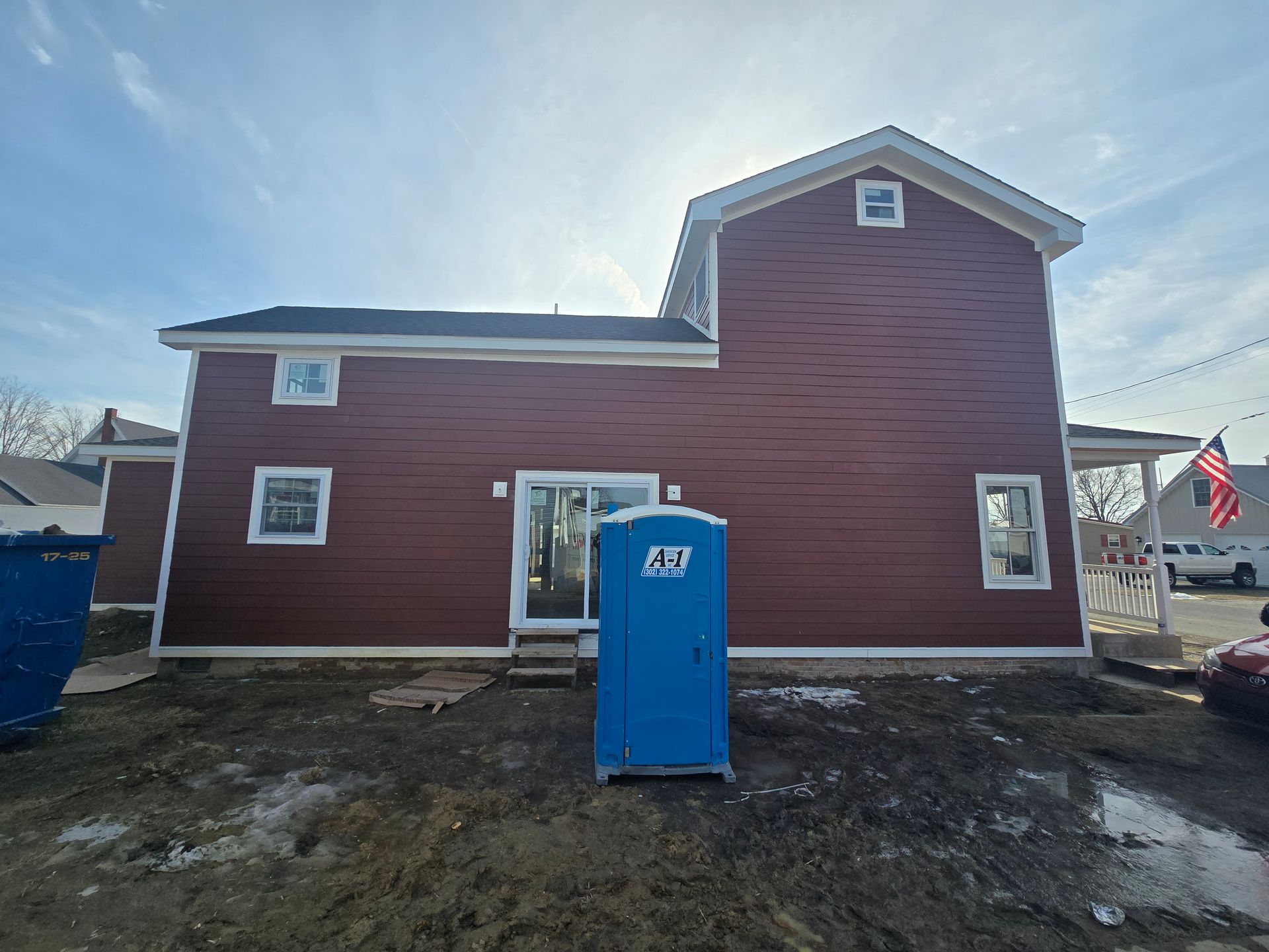 A blue portable toilet is sitting in front of a brown house.